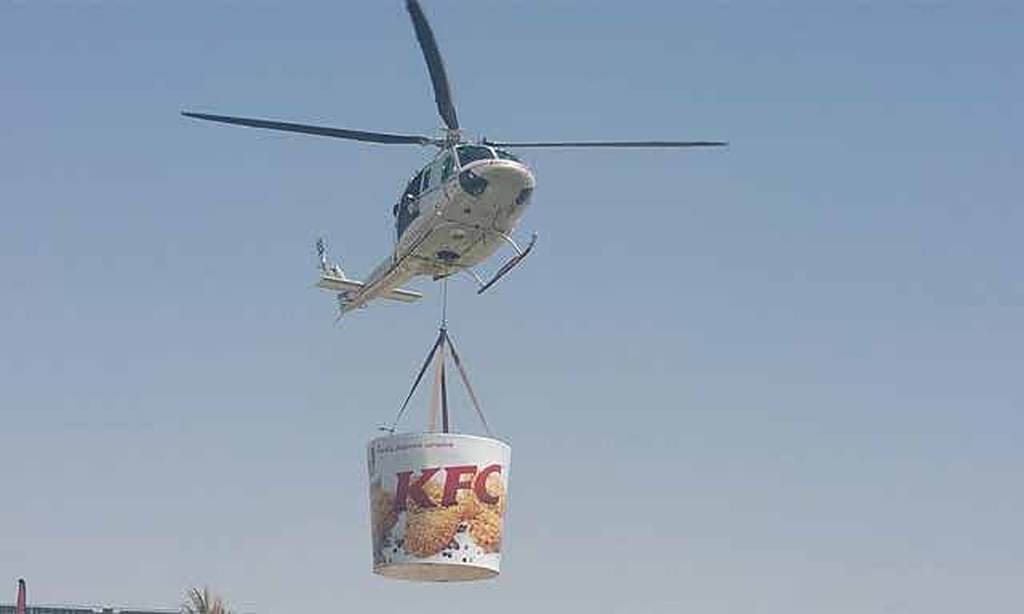 Helicopter carrying a giant KFC bucket over a park